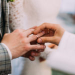 The close-up view of the priest putting the wedding ring on the finger of the groom.