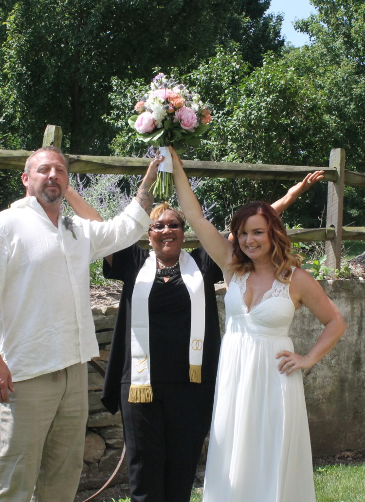 A wedding officiant posing for a picture with a just married couple
