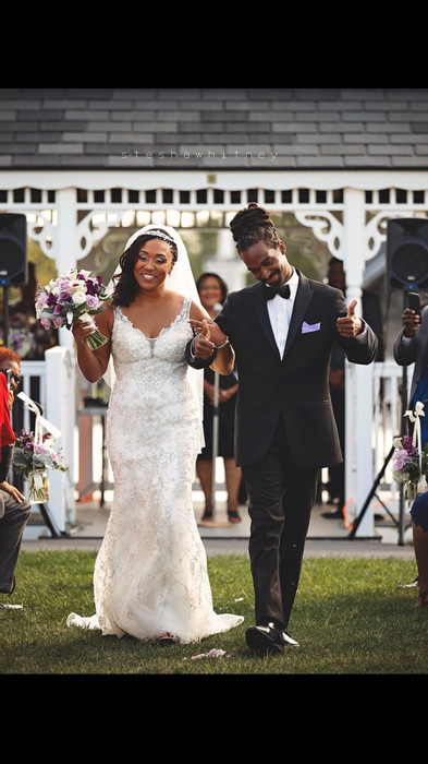 Happy couple walking down the aisle outside and holding hands up in the air